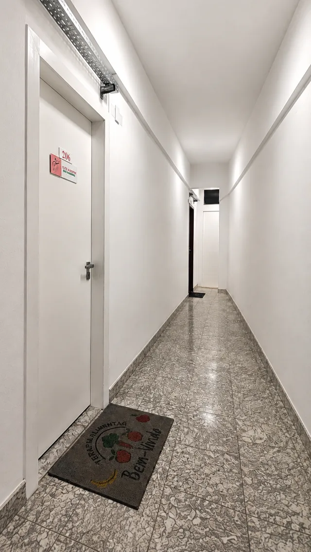 Corredor do edifício até a porta da sala 206, com tapete de boas-vindas na entrada